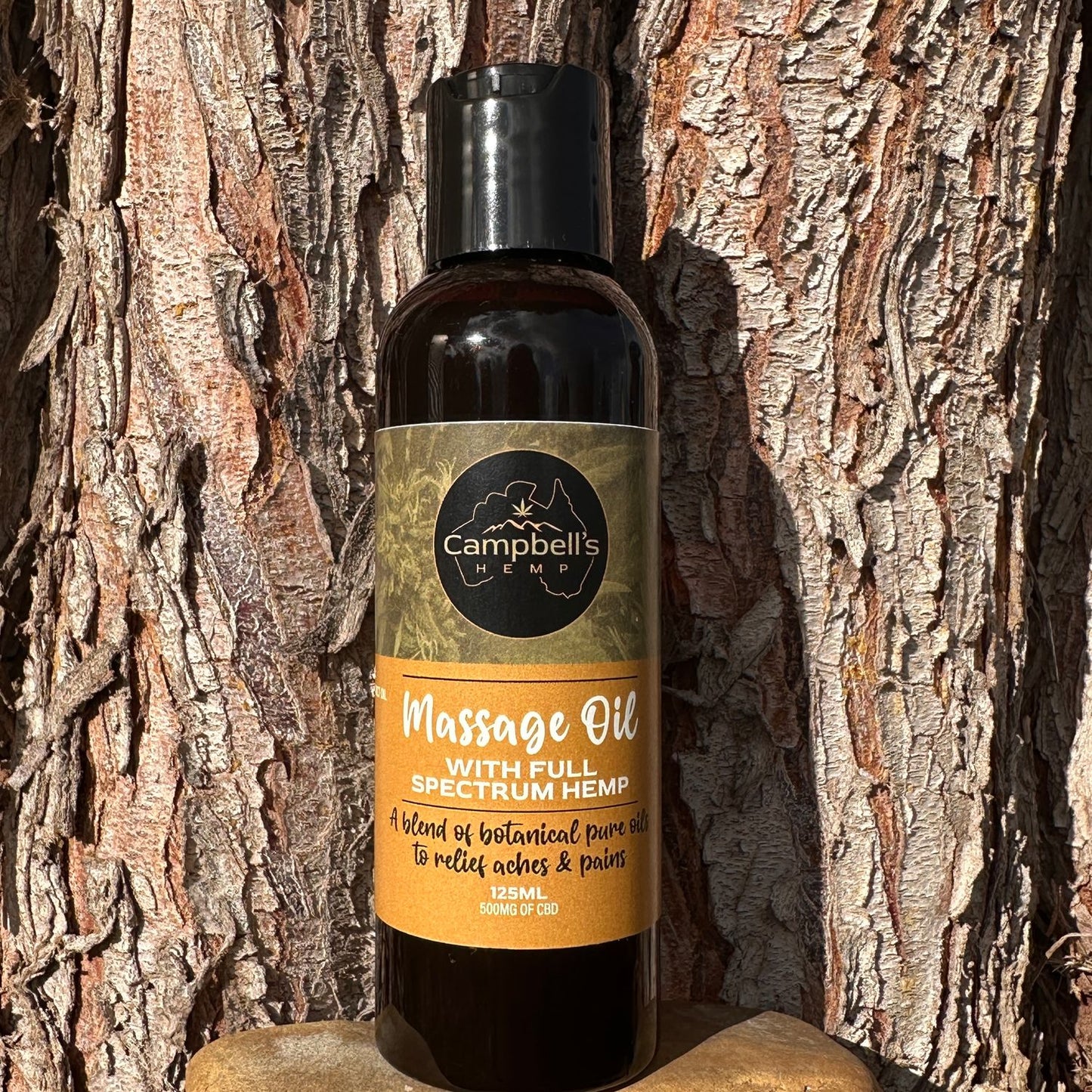 Campbell’s Hemp Massage Oil bottle displayed on natural oak wood, highlighting its earthy, organic ingredients and eco-friendly packaging in an outdoor setting.