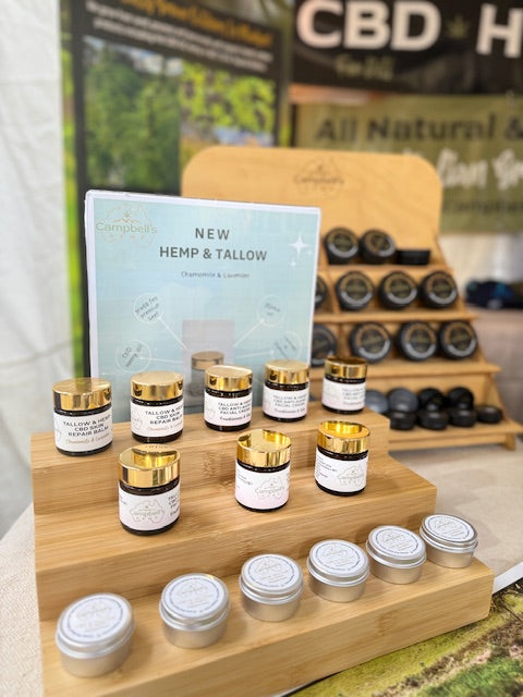 Display of Campbell’s Hemp & Tallow Chamomile & Lavender skincare balms in glass jars with gold lids and small tins, arranged on a wooden stand at a market stall.